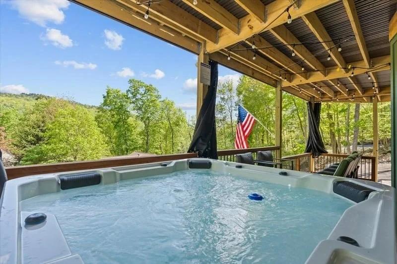 Private hot tub on a covered deck overlooking green mountain scenery